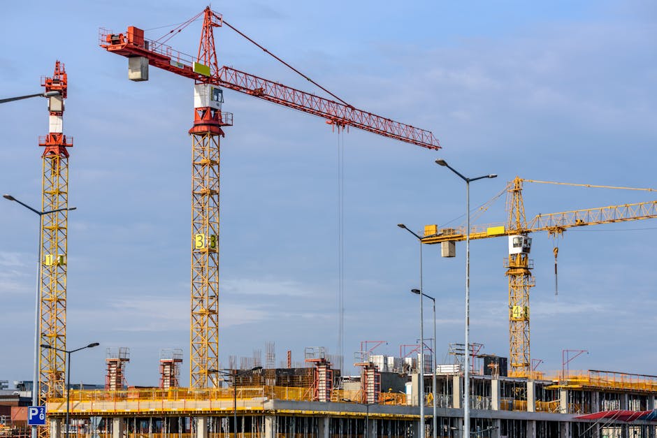 Multiple tower cranes working on a large construction site with blue sky backdrop